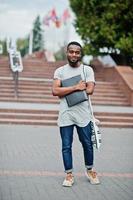 African student male posed with backpack and school items on yard of university, against flags of different countries. photo