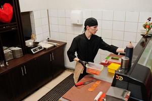 chef profesional vestido de negro haciendo sushi y rollos en la cocina de un restaurante de comida tradicional japonesa. foto