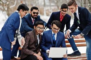 Group of six indian businessman in suits posed outdoor in winter day at Europe, looking on laptop. photo