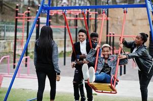 Young millennials african friends on playground, slide and swing. Happy black people having fun together. Generation Z friendship concept. photo