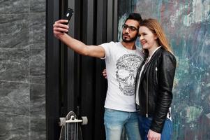 Cool multiracial couple posing against wall and making selfie together. photo