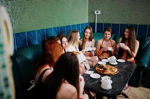 Group of eight sexy girls in swimsuits and bathrobe sitting in a bath and eating pizza. Girls rest friends. photo