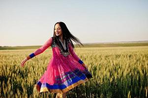 tierna niña india en sari, con maquillaje de labios violetas posada en el campo al atardecer. modelo indio de moda. foto