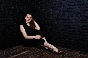 retrato de una hermosa morena con mono negro sentada y posando en el estudio. foto