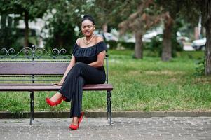 niña africana posó en la calle de la ciudad vestida de negro, sentada en el banco. foto