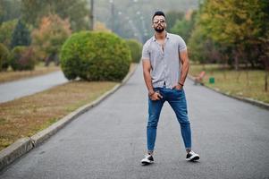 Fashionable tall arab beard man wear on shirt, jeans and sunglasses posed on park and hold wallet at hand. photo