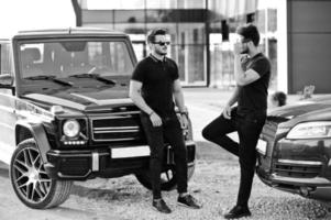 Two asian brothers man wear on all black posed near suv cars. photo