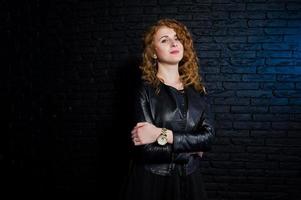 Curly hair girl at leather jacket on studio against black brick wall. photo