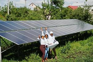 African american technician checks the maintenance of the solar panels. Group of three black engineers meeting at solar station. photo