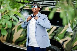 Stylish arabian man at sunglasses, cap and bow tie posed against military car. Arab model boy. photo