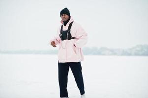 Elegante hombre afroamericano de estilo urbano con capucha rosa posado en un lago congelado en invierno. foto