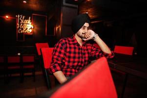 Indian man in checkered shirt and black turban sitting at bar. photo