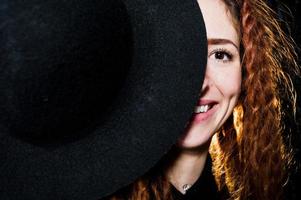 Studio shoot of girl in black with dreads and hat on brick background. photo