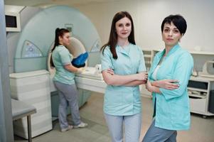 Three female doctors near magnetic resonance imaging machine with patient inside. photo