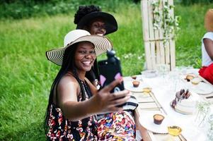 Group of african american girls celebrating birthday party outdoor with decor. Making selfie on phone. photo