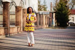 Stylish african american women in yellow jacket posed on street with hot drink in disposable paper cup. photo