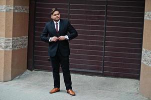 Stylish indian businessman in formal wear standing against brown shutter. photo