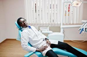 African american male doctor in glasses having rest after hard working day at dentist chair in dental clinic. photo