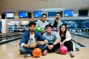 Group of five south asian peoples having rest and fun at bowling club, sitting on bowling alley with balls on hands. photo
