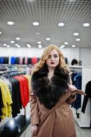 Elegance blonde girl in fur coat at the store of fur coats and leather jackets. photo