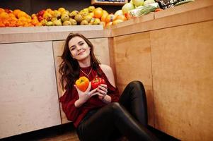 Girl in red holding two peppers on fruits store. photo