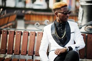 Chic handsome african american man in white suit and sunglasses sitting on bench. photo