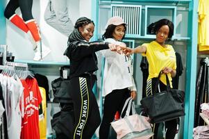 Three afican american women in tracksuits shopping with sport bags at sportswear mall against shelves. Sport store theme. photo