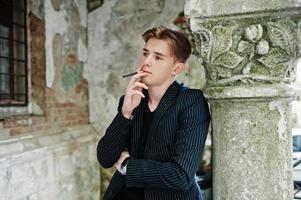 El joven macho usa una elegante chaqueta negra para fumar cigarrillos en las calles. foto