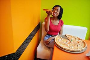African woman with pizza sitting at bright colored restaurant. photo