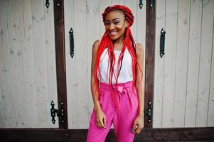 chica afroamericana de moda en pantalones rosas y rastas rojas posadas al aire libre. foto