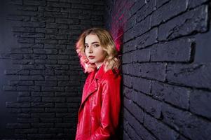 retrato de estudio de una chica rubia con una chaqueta de cuero roja contra una pared de ladrillos. foto