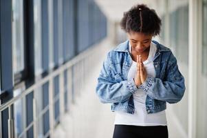 African woman in jeans jacket pray indoor. photo