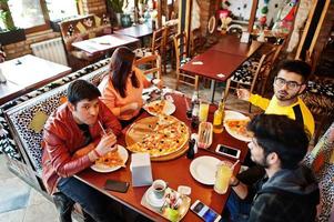 grupo de amigos asiáticos comiendo pizza durante la fiesta en la pizzería. gente india feliz divirtiéndose juntos, comiendo comida italiana y sentados en el sofá. foto