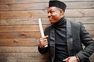 Strong powerful african american man in black suit and turtleneck and cap, with elephant tusk. photo