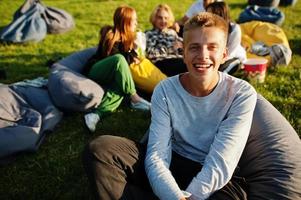 Young multi ethnic group of people watching movie at poof in open air cinema. Close up portrait of funny guy. photo