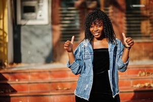 Stylish trendy afro france curly woman posed at autumn day in jeans jacket. Black african female model show thumbs up. photo