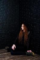 Studio shoot of girl in black with dreads, at glasses and hat on brick background. photo