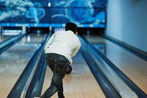 Back of asian man in jeans shirt standing at bowling alley with ball on hands and throw it. photo