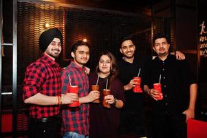 Group of indian friends having fun and rest at night club, drinking cocktails. photo