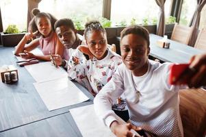 Happy african friends sitting and chatting in cafe. Group of black peoples meeting in restaurant and look at their mobile phone. photo