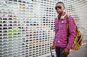 hombre afroamericano con camisa a cuadros, gafas de sol y jeans con maleta y mochila. viajero hombre negro libre de impuestos. foto