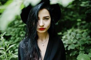 Close up portrait of sensual girl all in black, red lips and hat. Goth dramatic woman. photo