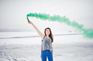 niña con bomba de humo de color verde en la mano en el día de invierno. foto