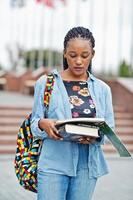 African student female posed with backpack and school items on yard of university, against flags of different countries. photo