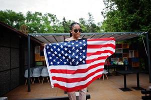 elegante mujer afroamericana con gafas de sol posadas al aire libre con la bandera de estados unidos. foto