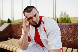 joven musculoso barbudo brutal vestido con traje deportivo blanco con camisa roja. foto