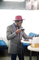 Stylish African American man model in gray jacket tie and red hat drink coffee at cafe and read newspapers. photo