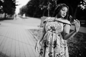 linda chica afroamericana de pequeña altura con rastas, vestida con un vestido amarillo de color, posada al atardecer. en blanco y negro. foto