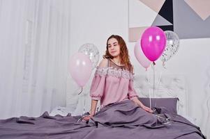 Young girl with balloons on bed posed on studio room. photo