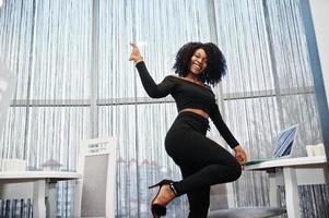 Fashionable young beautiful african american business woman with afro hairstyle wear in elegant black, stand with laptop. photo